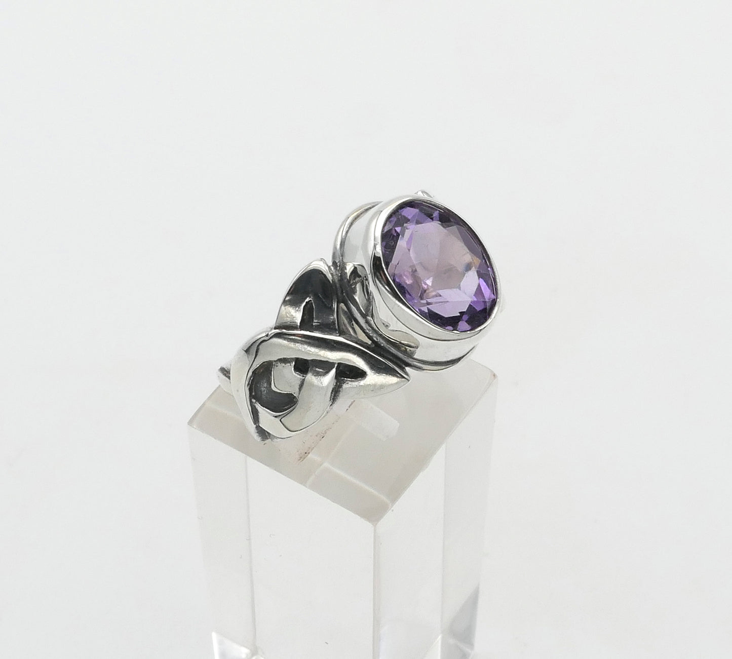 Silver ring with a purple gemstone on a clear stand against a white background
