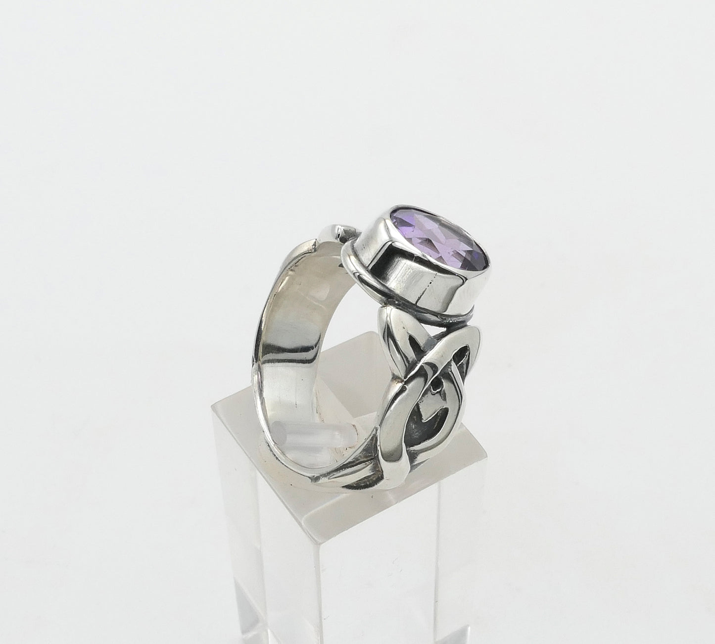Silver ring with a purple gemstone on a clear stand against a white background