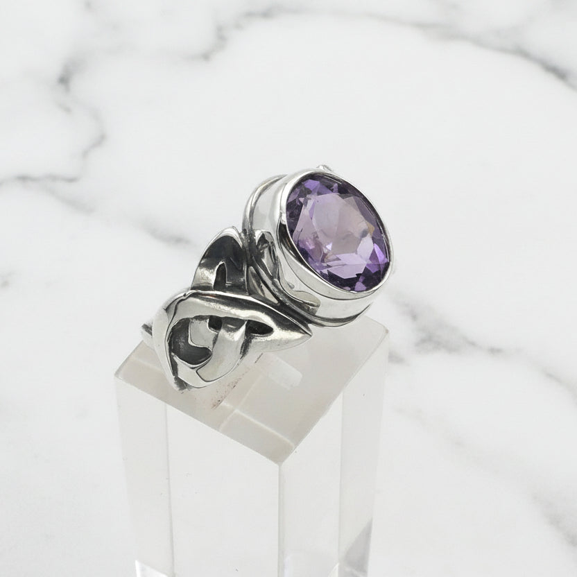Silver ring with a purple gemstone on a clear stand against a white background