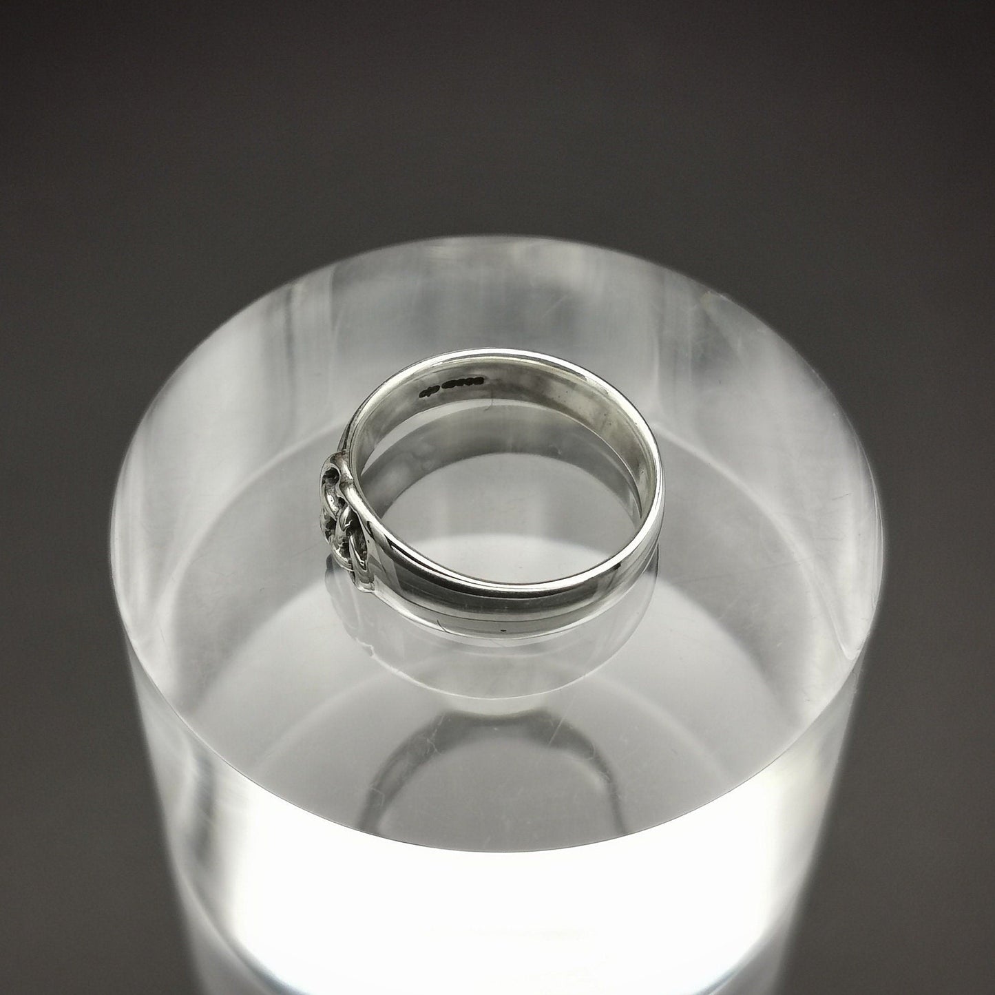 Silver ring on a clear cylindrical stand against a dark background