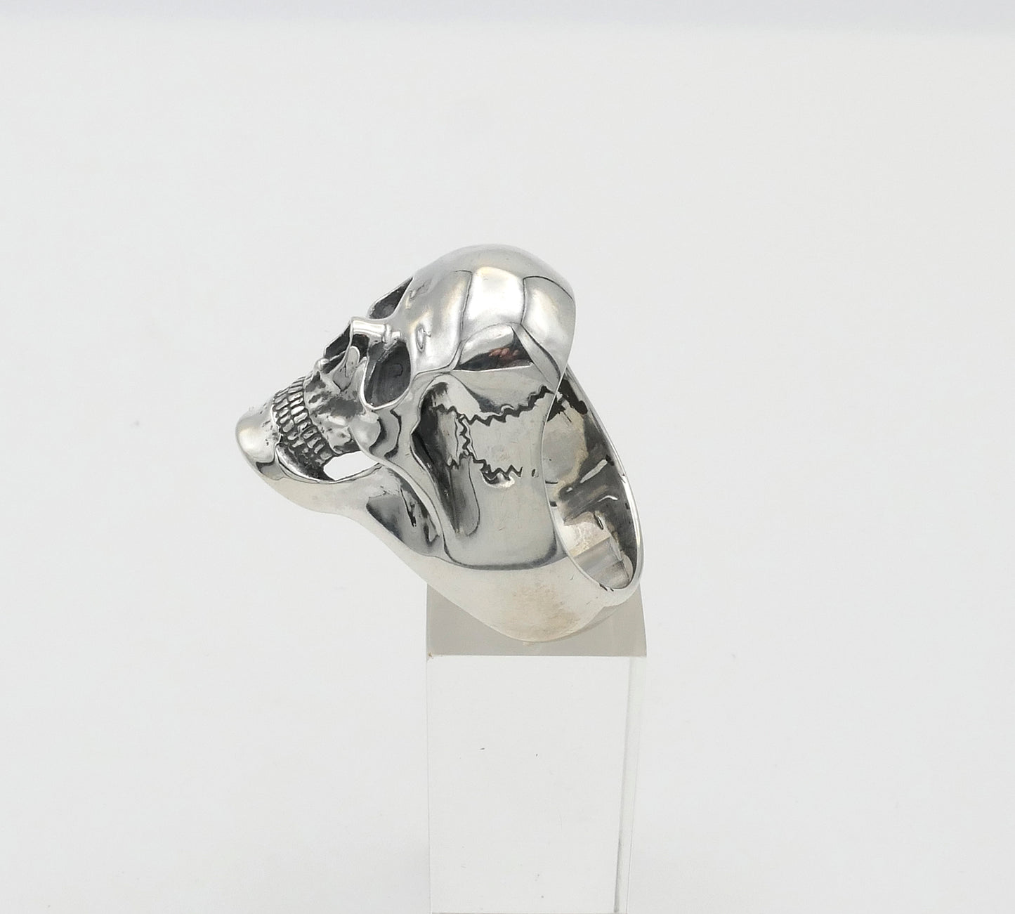 Silver skull-shaped ring on a white stand with a white background