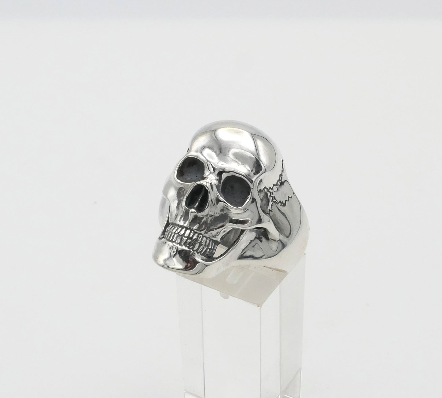 Silver skull ring on a clear stand with a white background