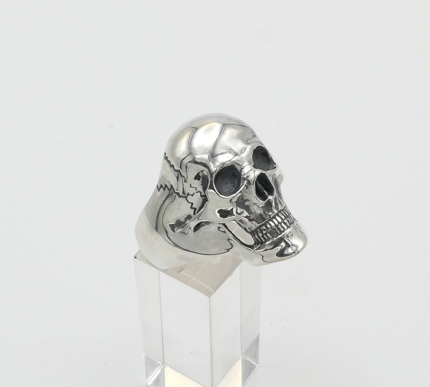 Silver skull ring on a clear stand against a white background