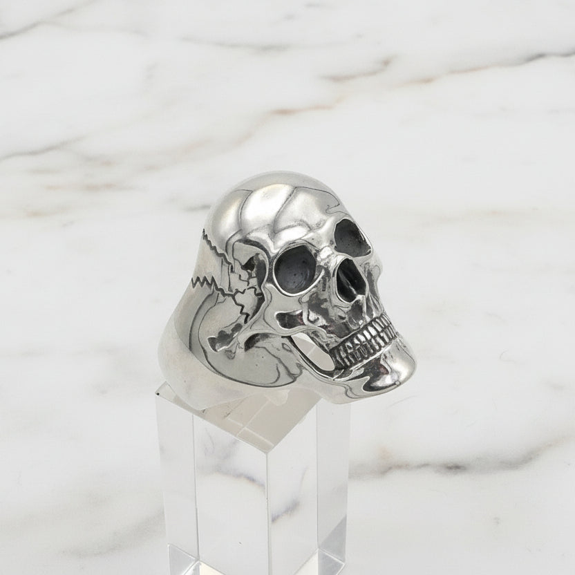Silver skull ring on a clear stand against a white background