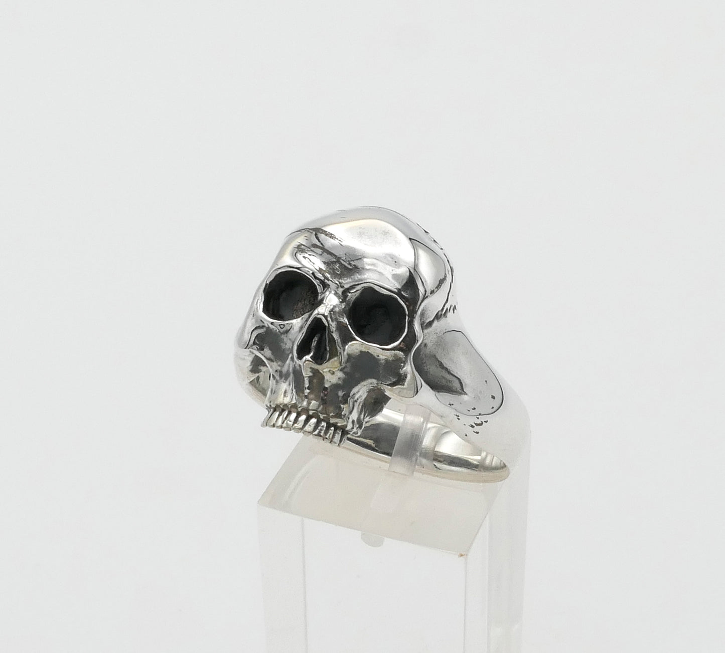 Silver skull ring on a clear stand against a white background