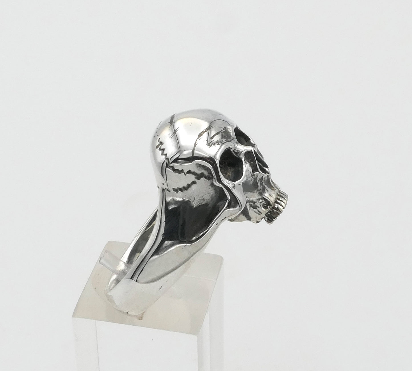 Silver skull-shaped ring on a clear stand against a white background