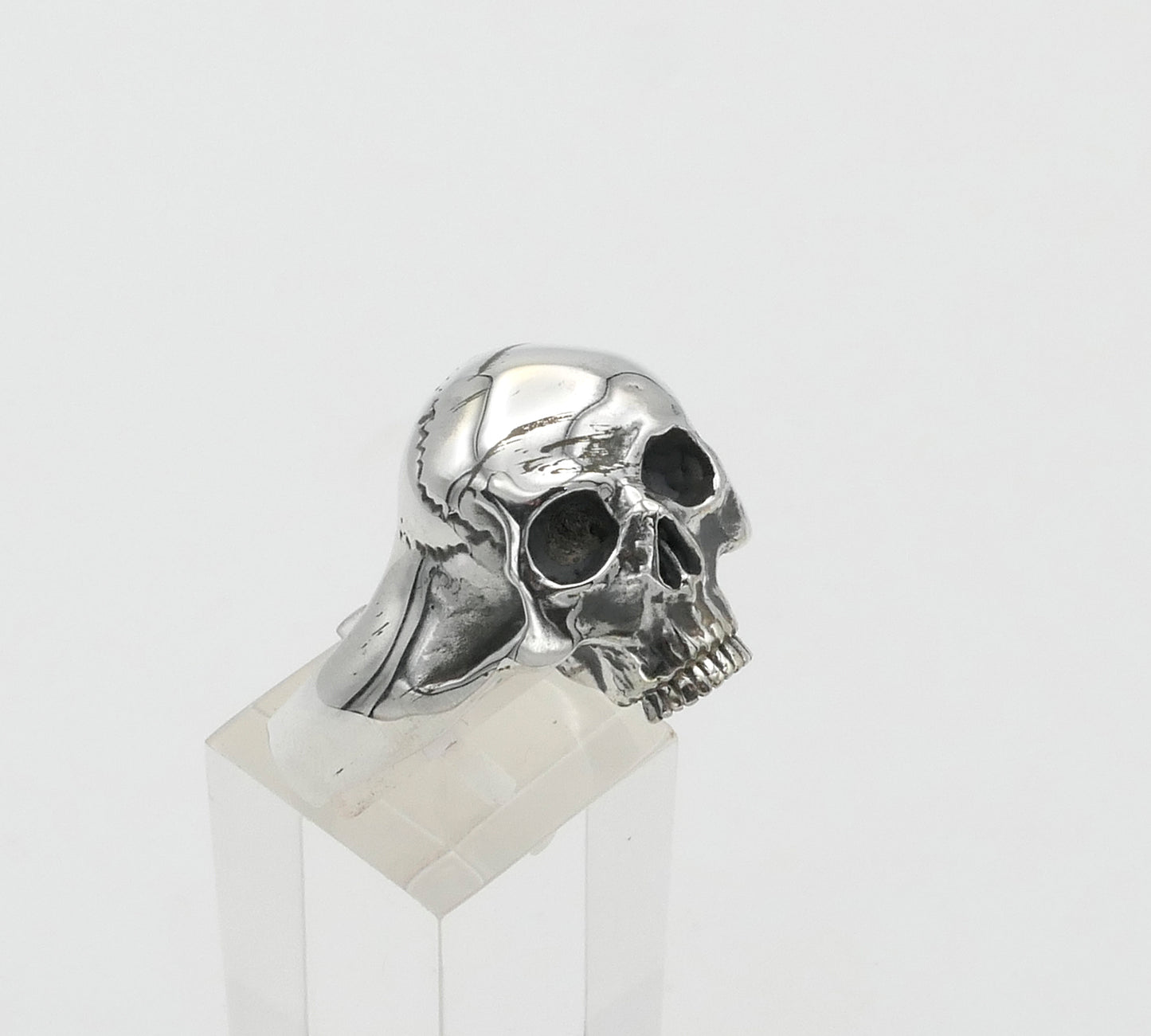 Silver skull ring on a clear stand with a white background