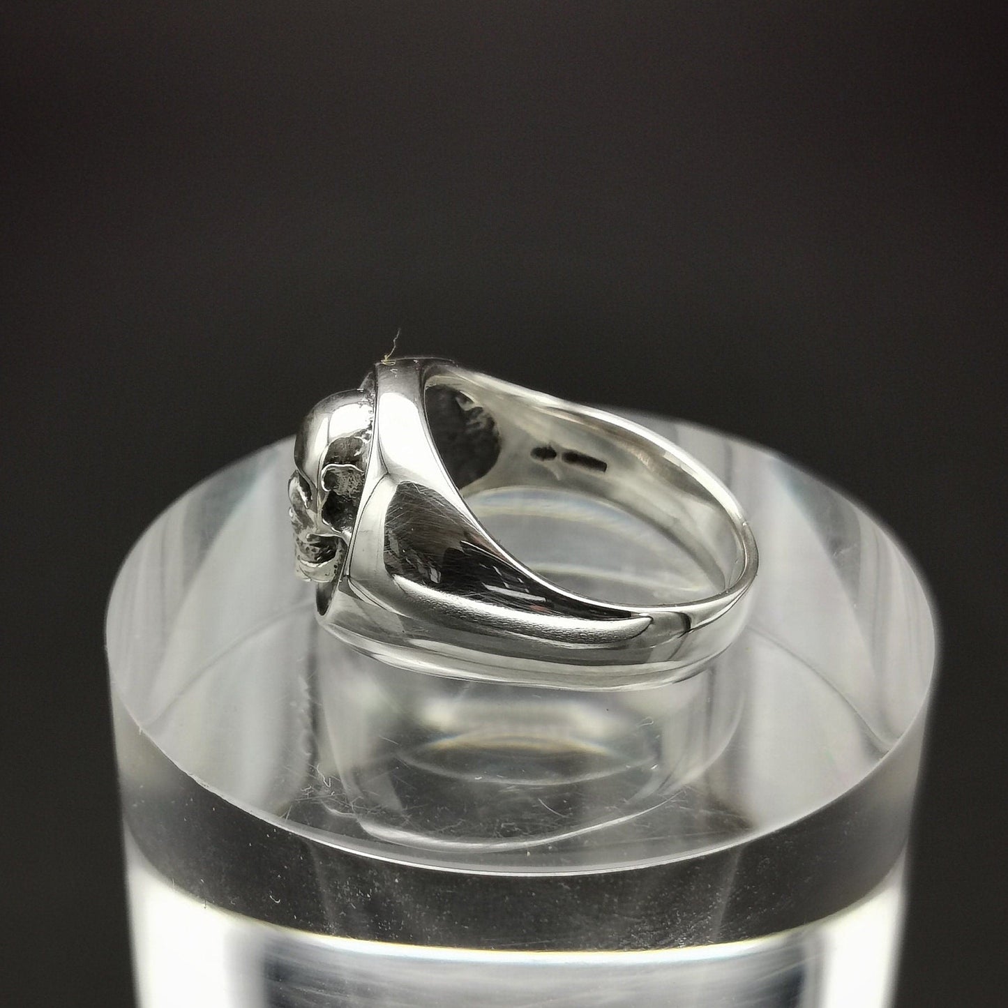 Silver ring on a clear stand with a black background