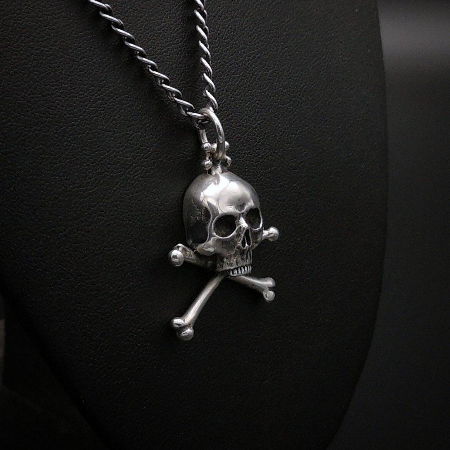 Silver skull and crossbones pendant on a chain against a dark background