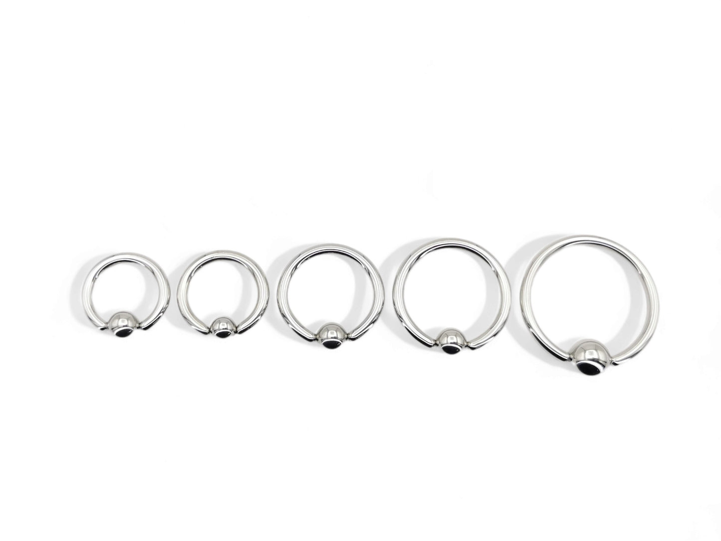 A collection of surgical steel ball closure rings in various sizes, with a polished metallic finish.
