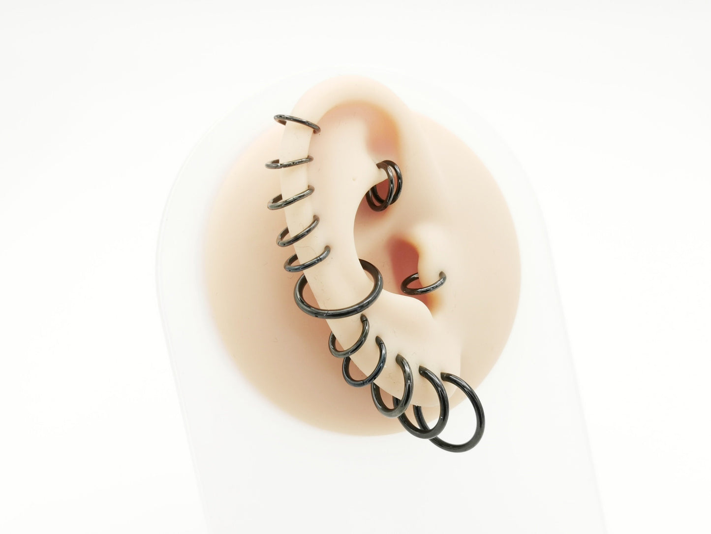 A collection of black surgical steel clicker rings for ear and nose piercings, worn on a mannequin ear