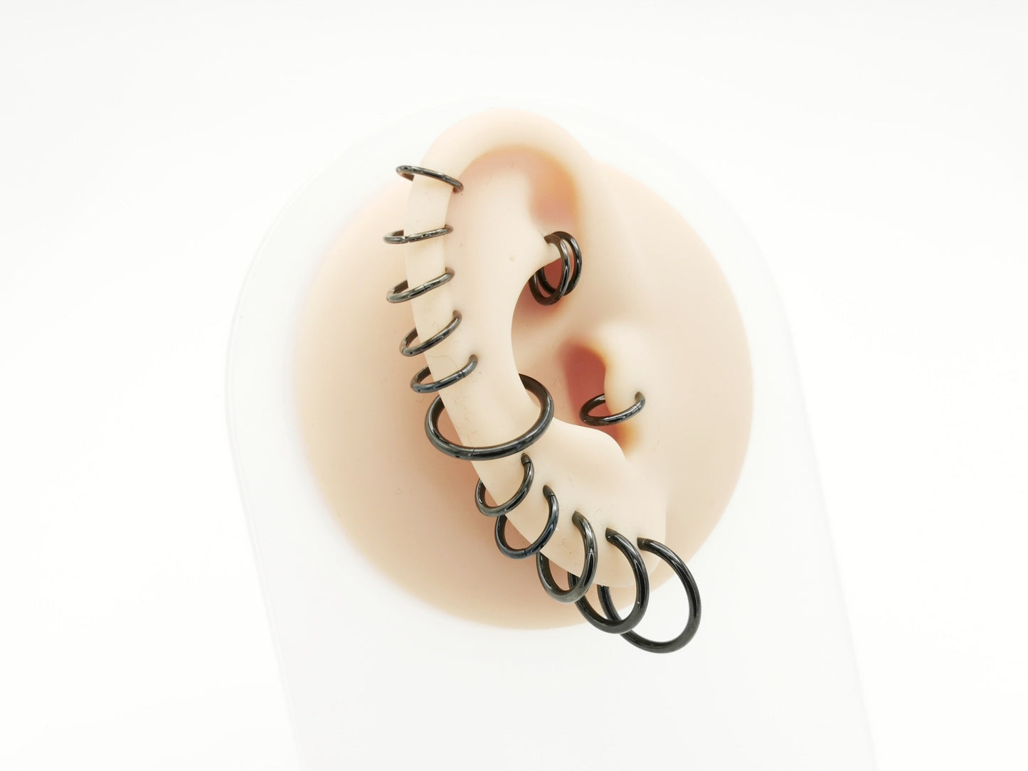 A set of black surgical steel clicker rings arranged in parallel worn on a mannequin ear