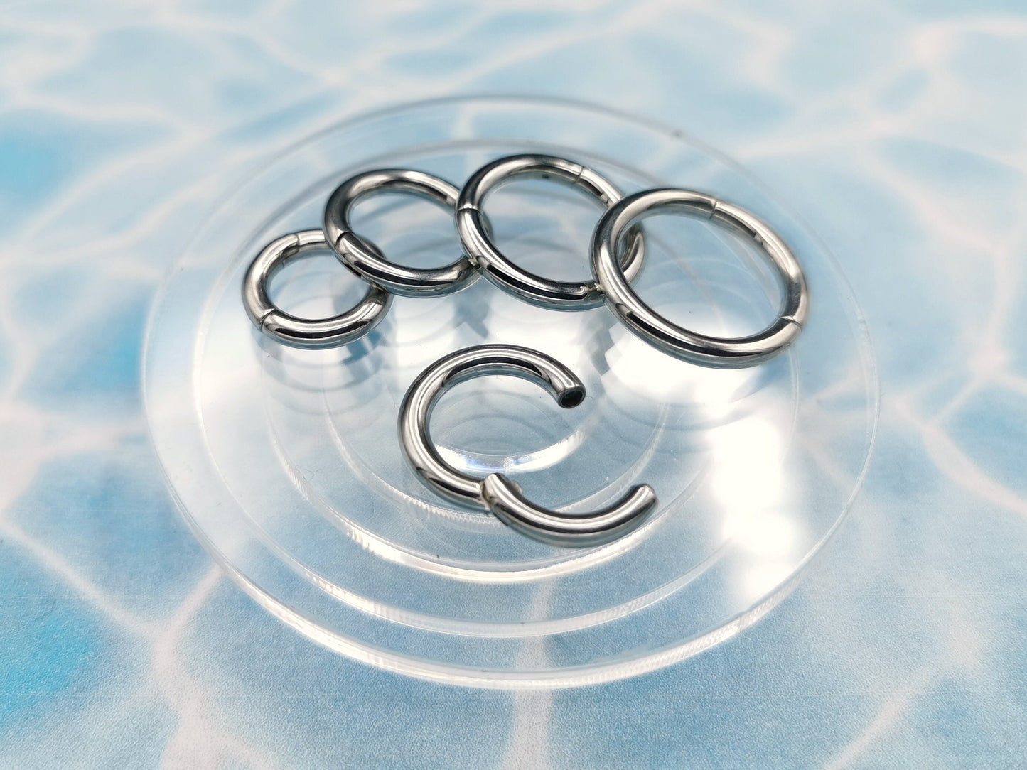 A set of four silver surgical steel clicker rings for body piercing, displayed on a blue background.