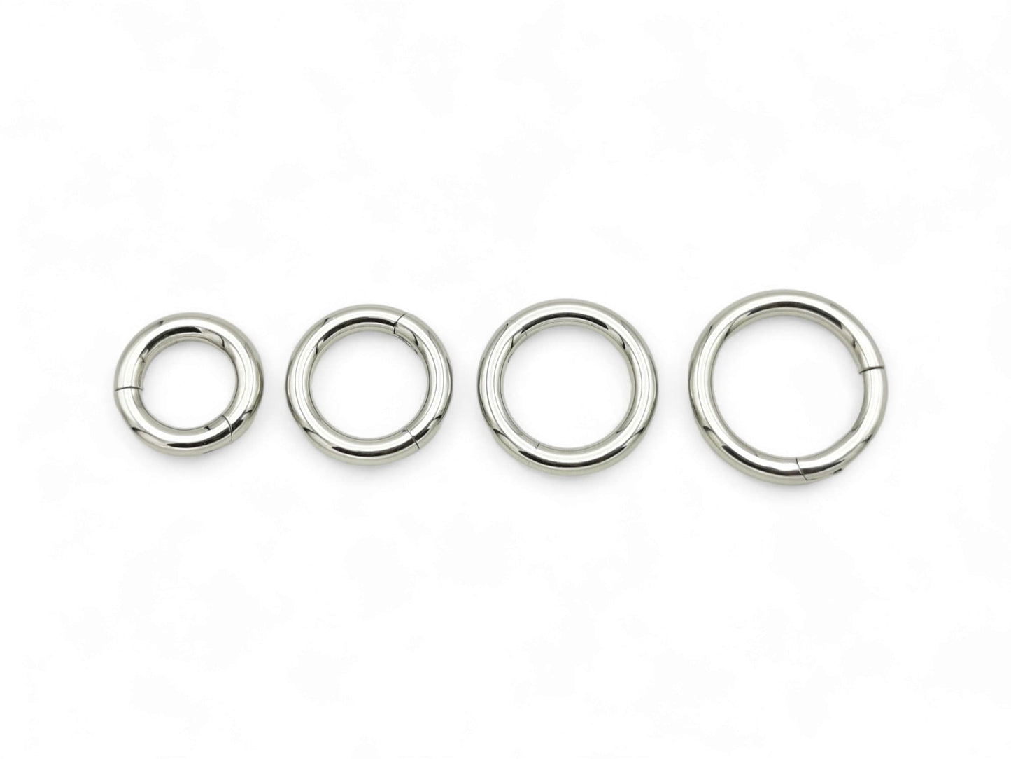 Three silver surgical steel clicker rings of different sizes arranged side by side against a white background.