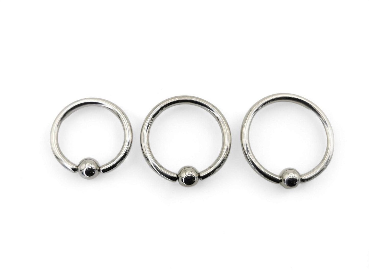 A collection of polished titanium BCRs with a ball/bead closure, displayed in two overlapping rows with varying diameters.