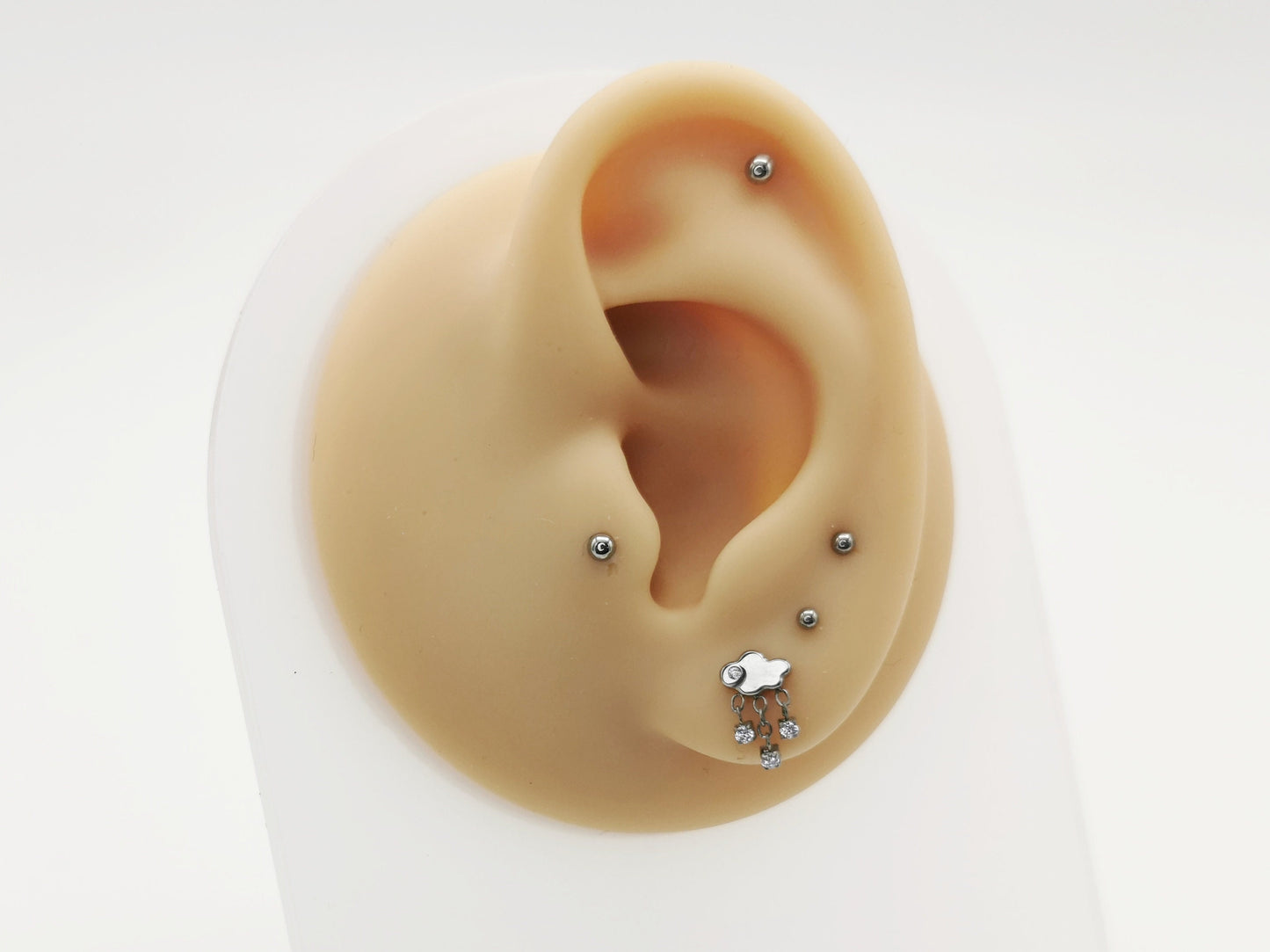 A silver-colored titanium threadless stud with a rain cloud shape and three jewelled rain drops, placed on a white background.