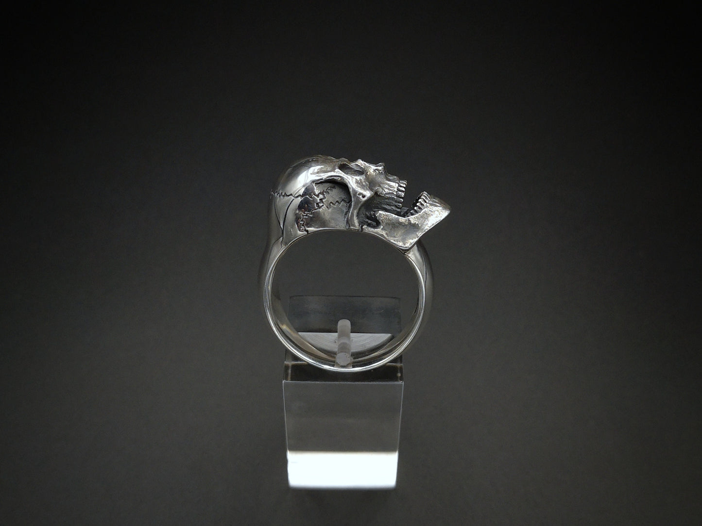 A silver screaming skull ring displayed on a clear stand, with a detailed human skull design around the finger.