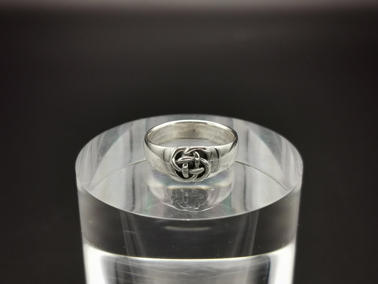 A sterling silver Celtic knot ring with a small knot design, displayed on a clear stand.