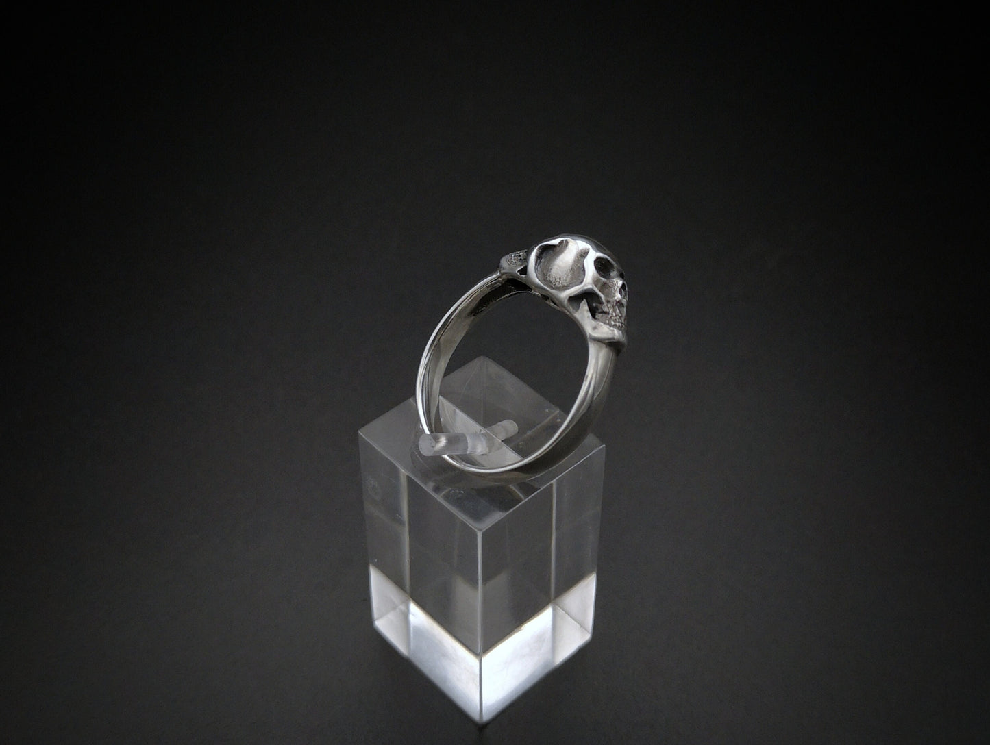 Sterling silver ring with twin skull design displayed on a clear stand against a black background.
