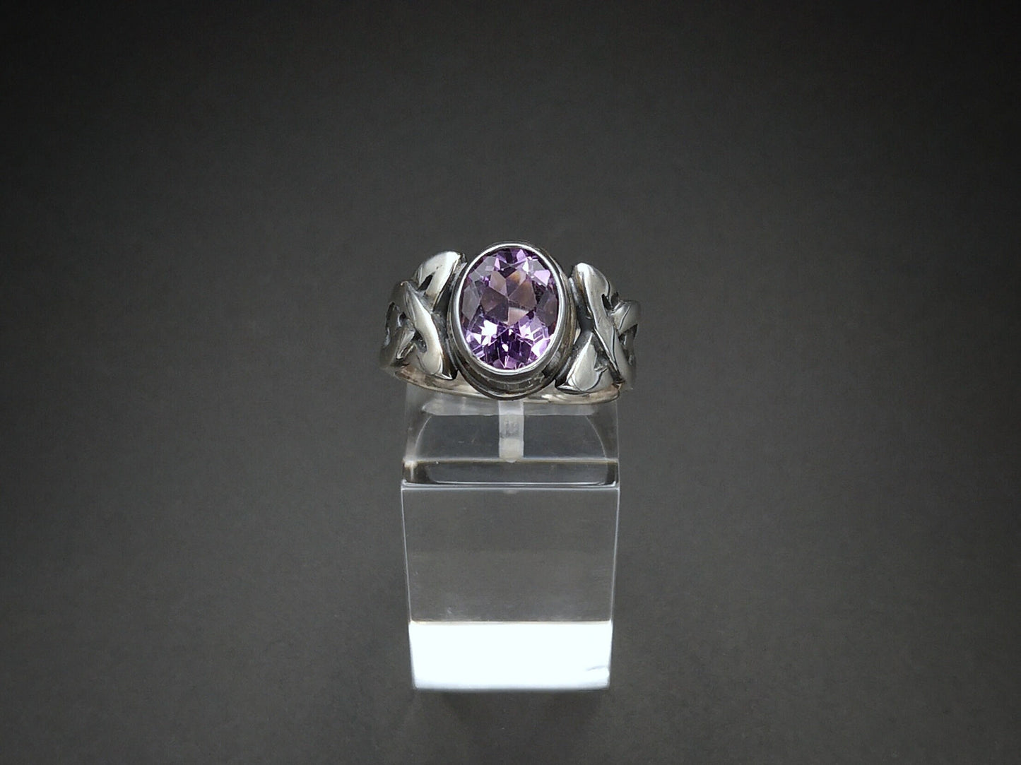A sterling silver Celtic ring with a bezel-set amethyst, displayed on a clear stand.