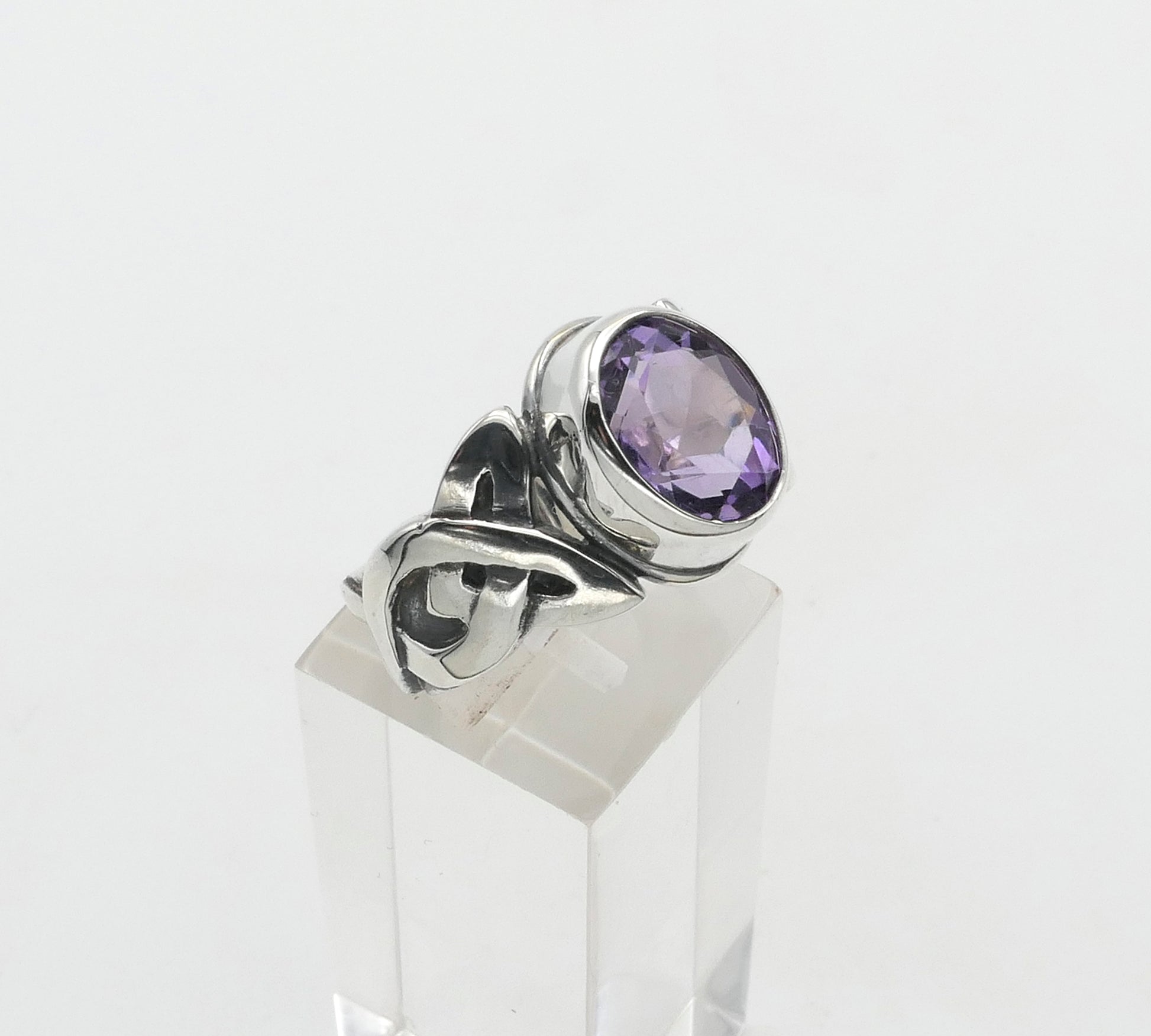 Silver ring with a purple gemstone on a clear stand against a white background