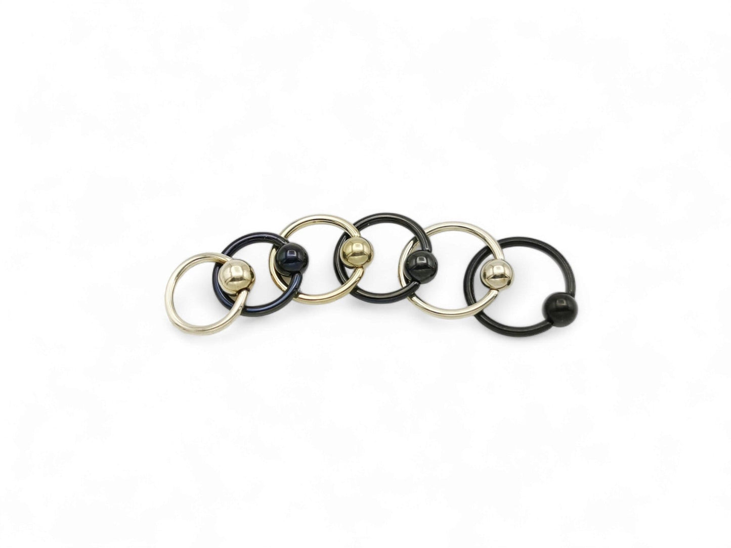 A collection of black and gold titanium BCRs with a 4mm ball closure design, displayed against a white background.