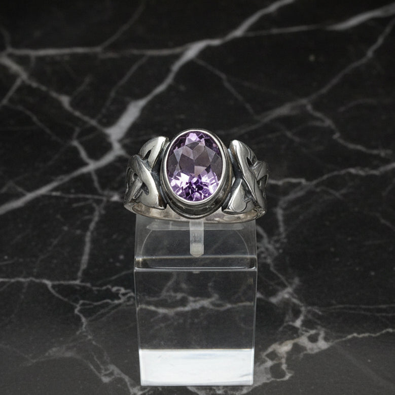 A sterling silver Celtic ring with a bezel-set amethyst, displayed on a clear stand.