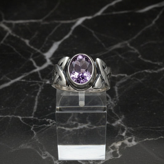 A sterling silver Celtic ring with a bezel-set amethyst, displayed on a clear stand.
