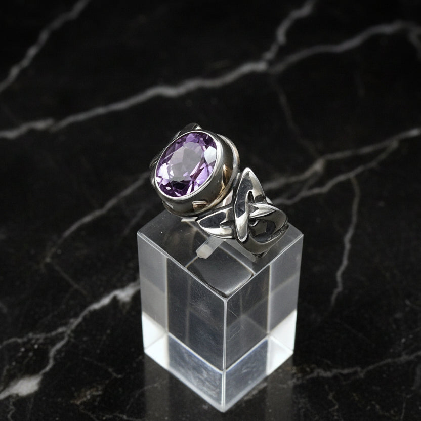 Silver ring with a purple gemstone on a clear stand against a dark marble background