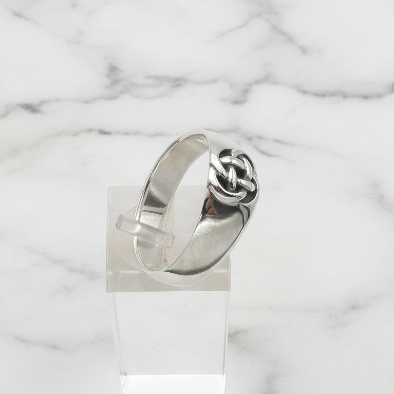 Silver ring with a knot design on a clear stand against a white background