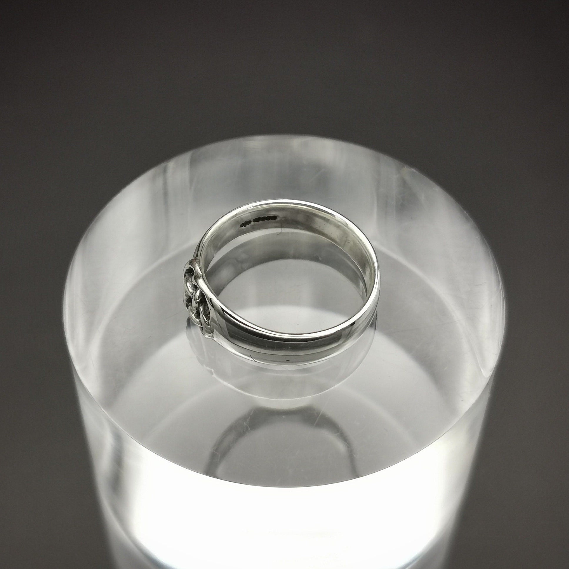 Silver ring on a clear cylindrical stand against a dark background