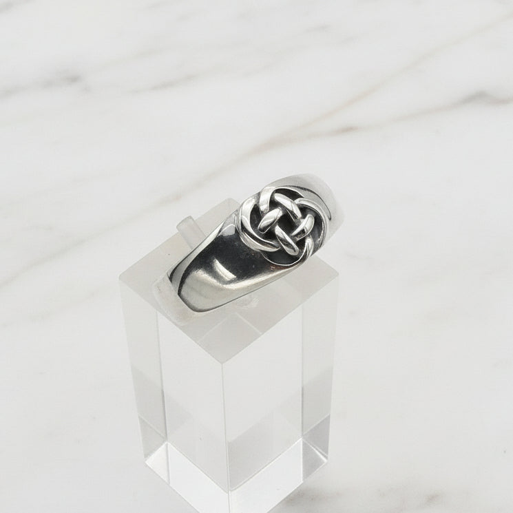 Silver ring with a knot design on a clear stand against a white background