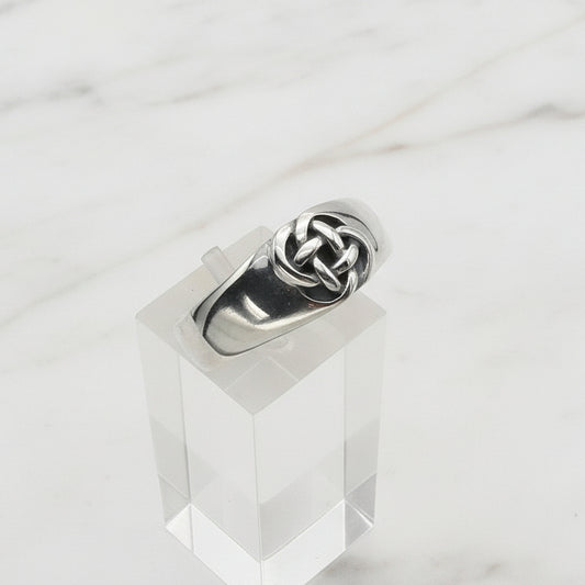 Silver ring with a knot design on a clear stand against a white background