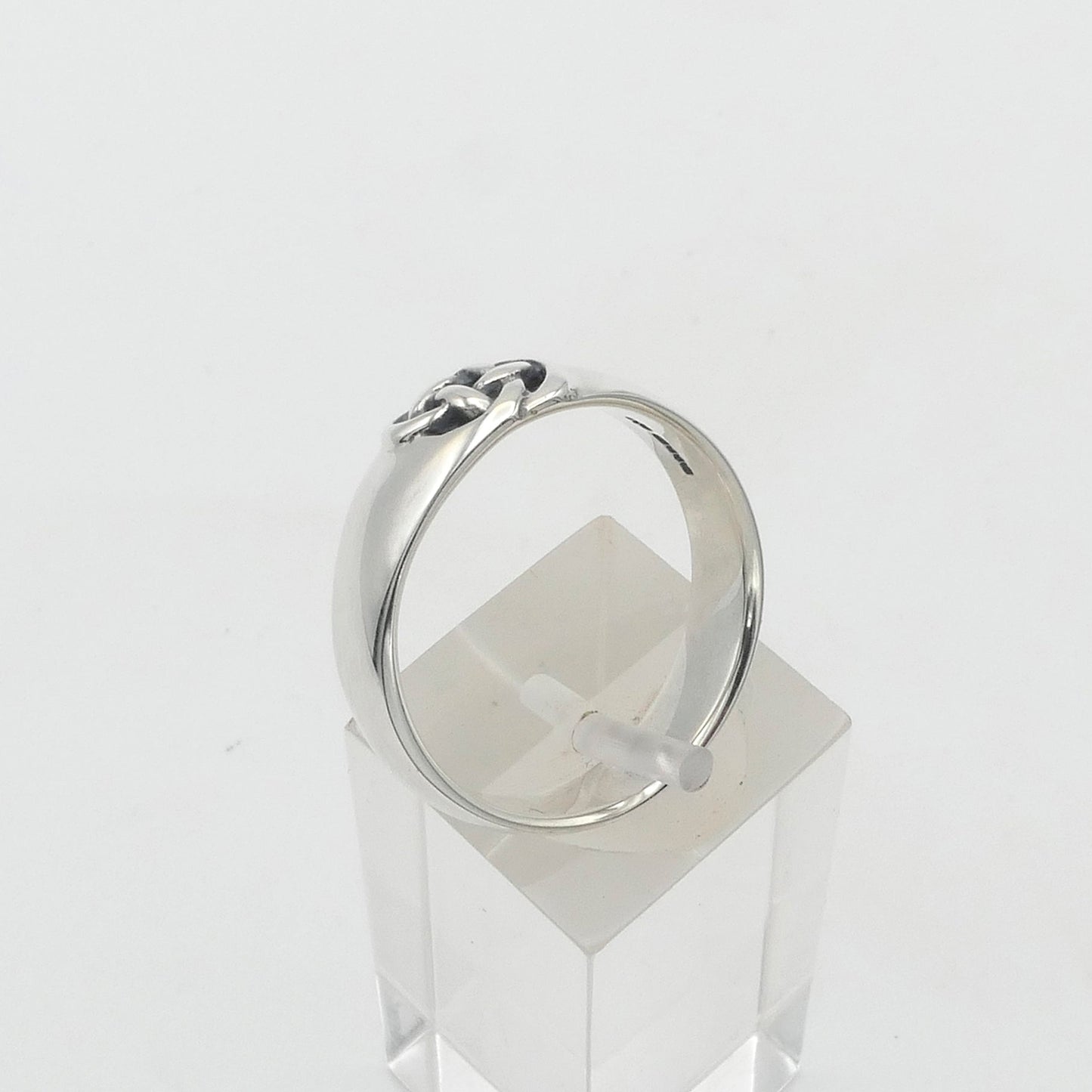 Silver celtic knot ring on a clear stand against a white background