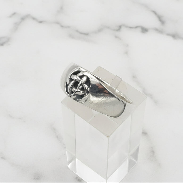 Silver celtic knot ring on a clear stand against a white background