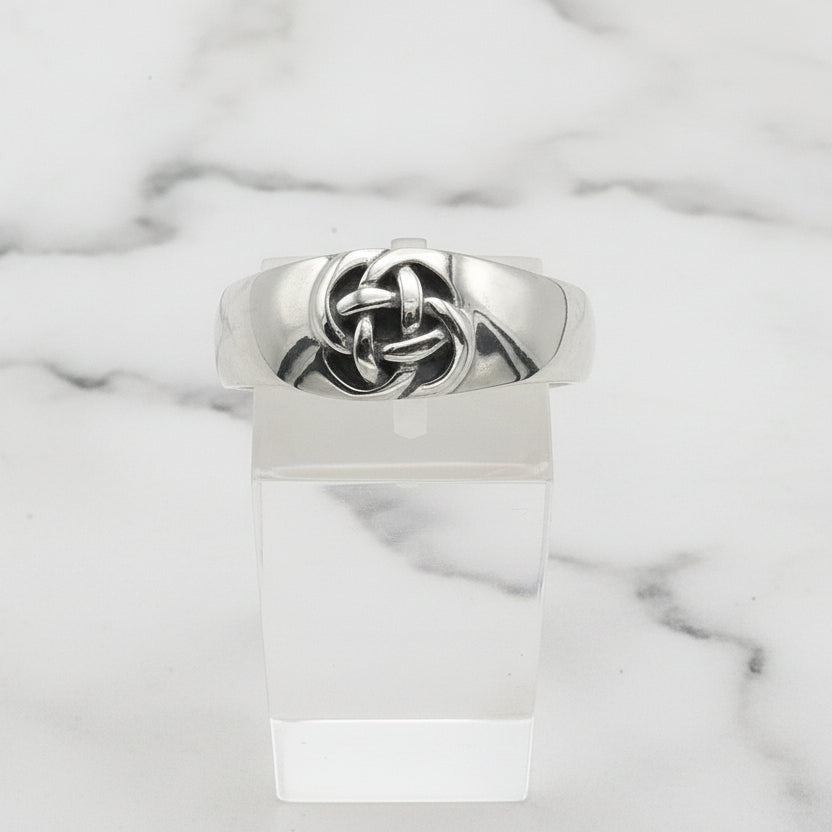 Silver ring with a knot design on a clear stand against a white background