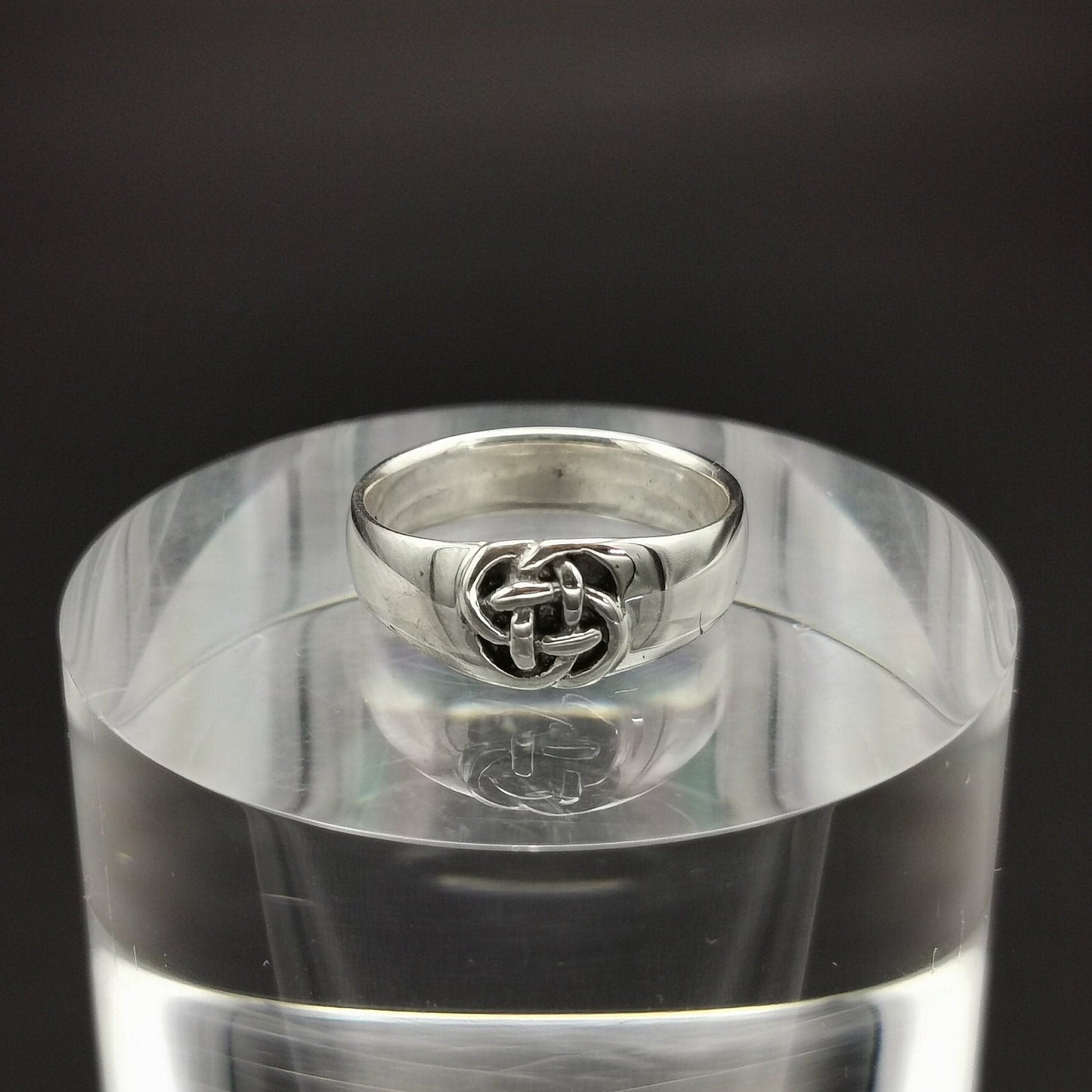 A sterling silver Celtic knot ring with a small knot design, displayed on a clear stand.