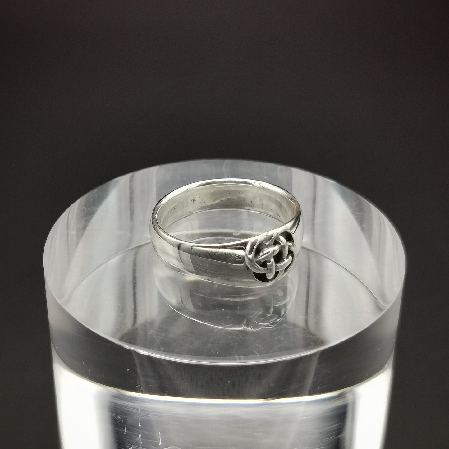 Silver ring on a clear acrylic stand against a black background