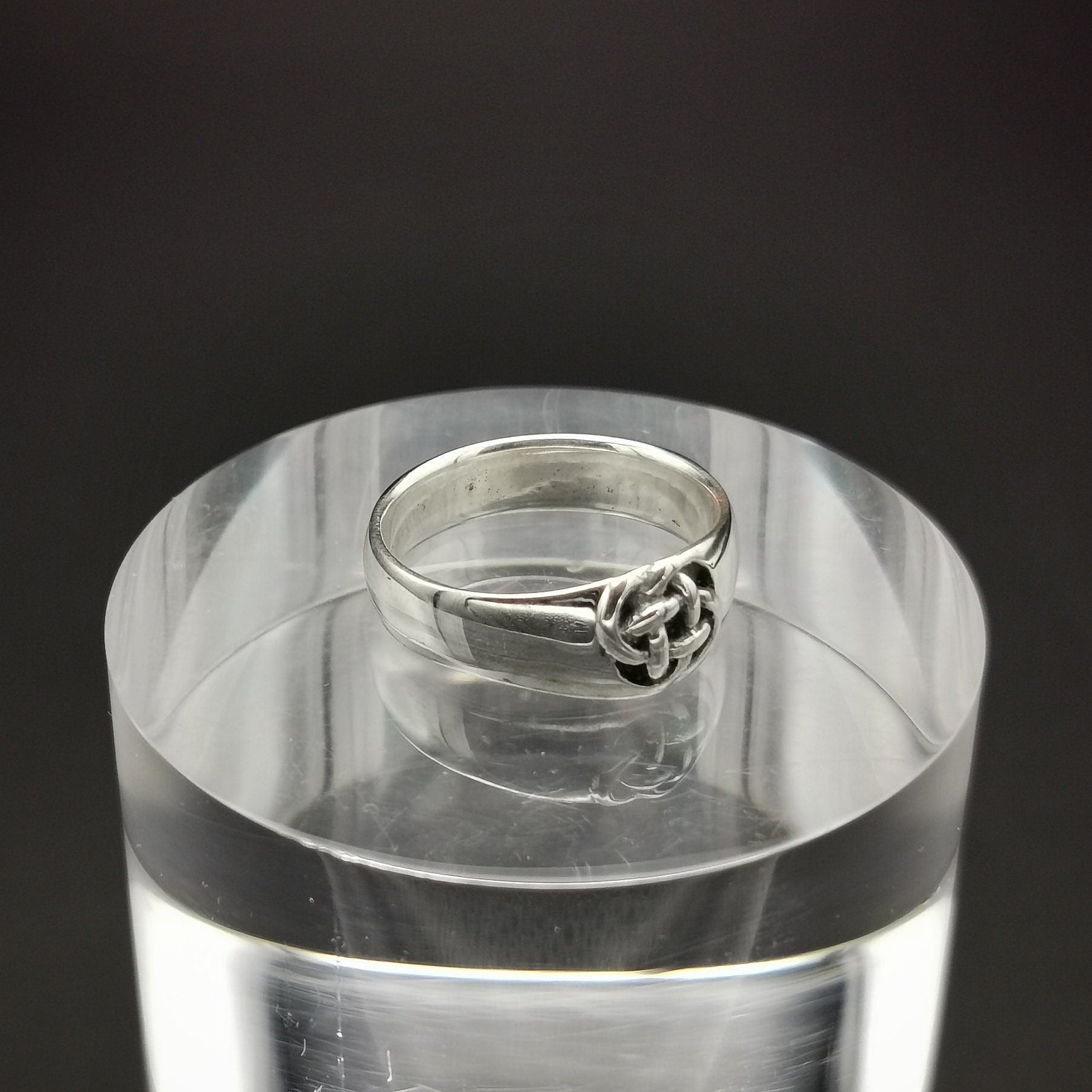 Silver ring on a clear acrylic stand against a black background