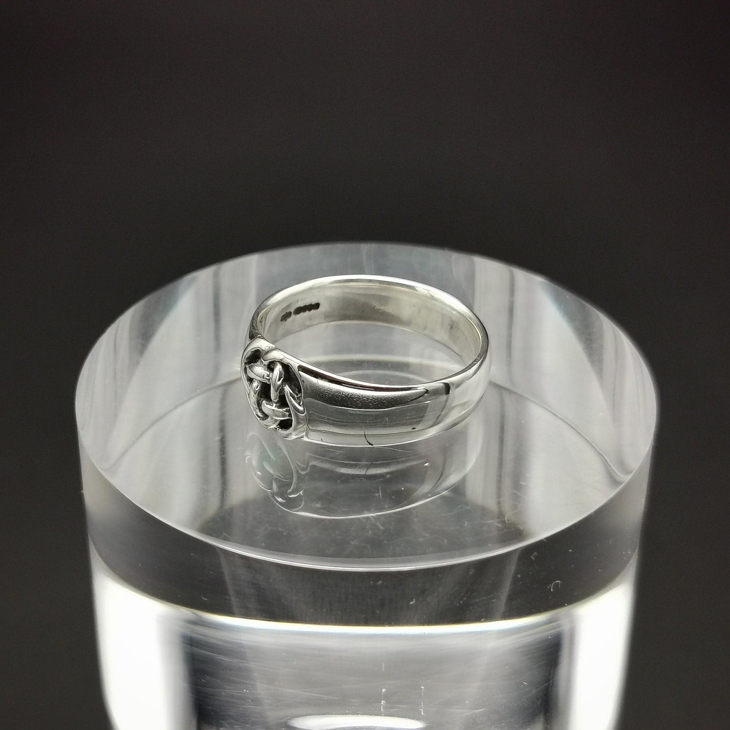 Silver ring on a clear acrylic stand against a black background