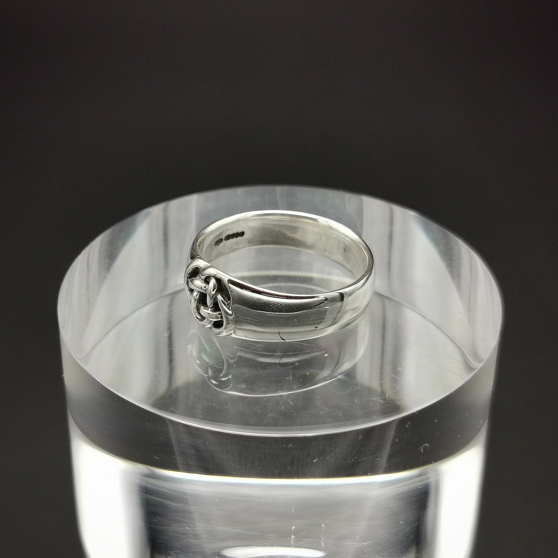 Silver ring on a clear acrylic stand against a black background