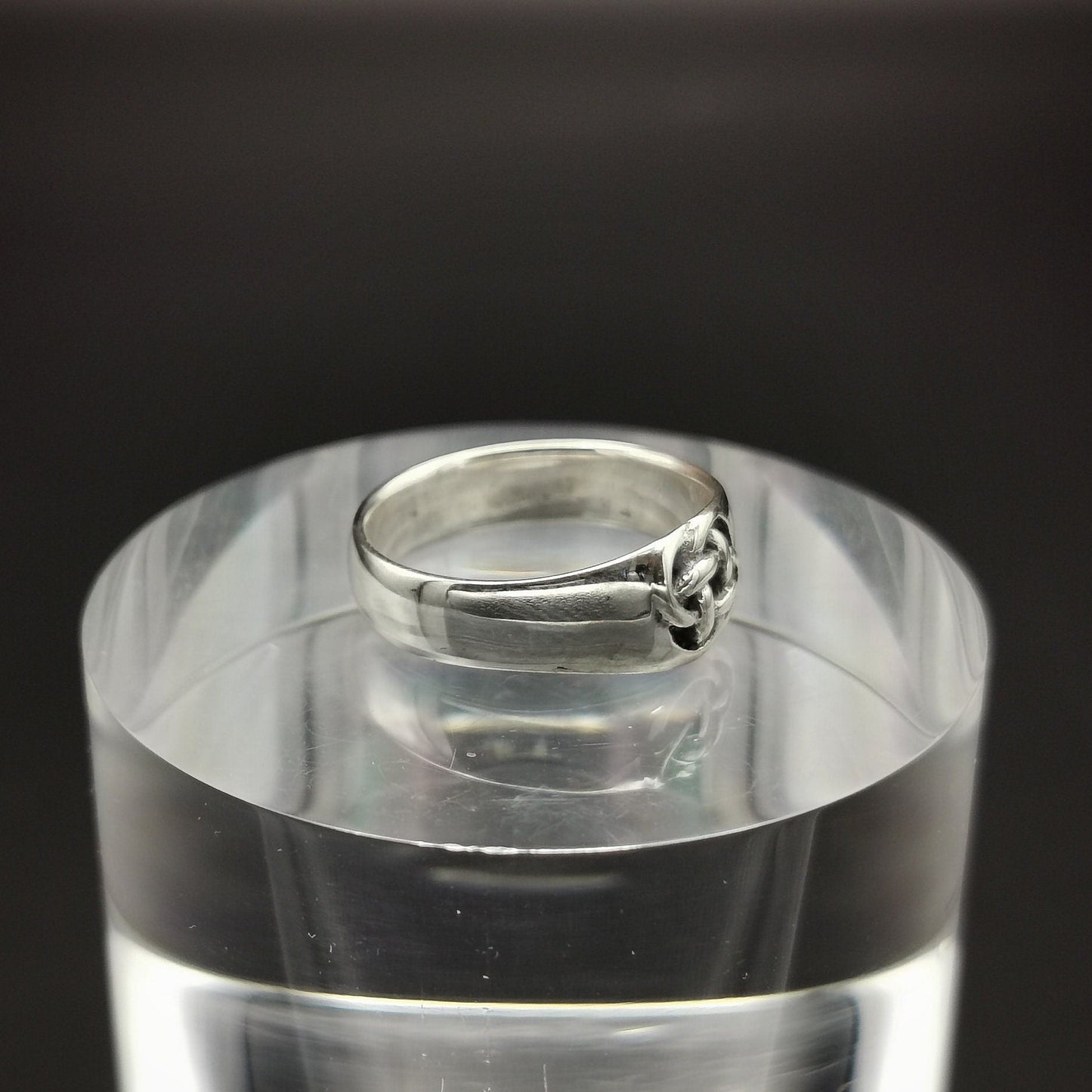 Silver ring on a clear stand with a black background