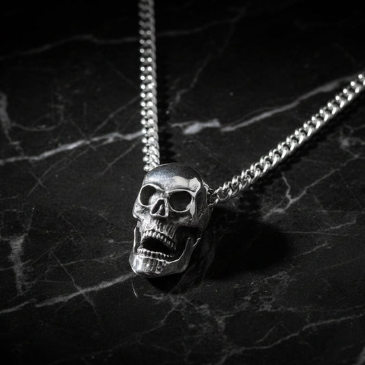 A silver skull pendant necklace with a silver curb chain, displayed on a mannequin.