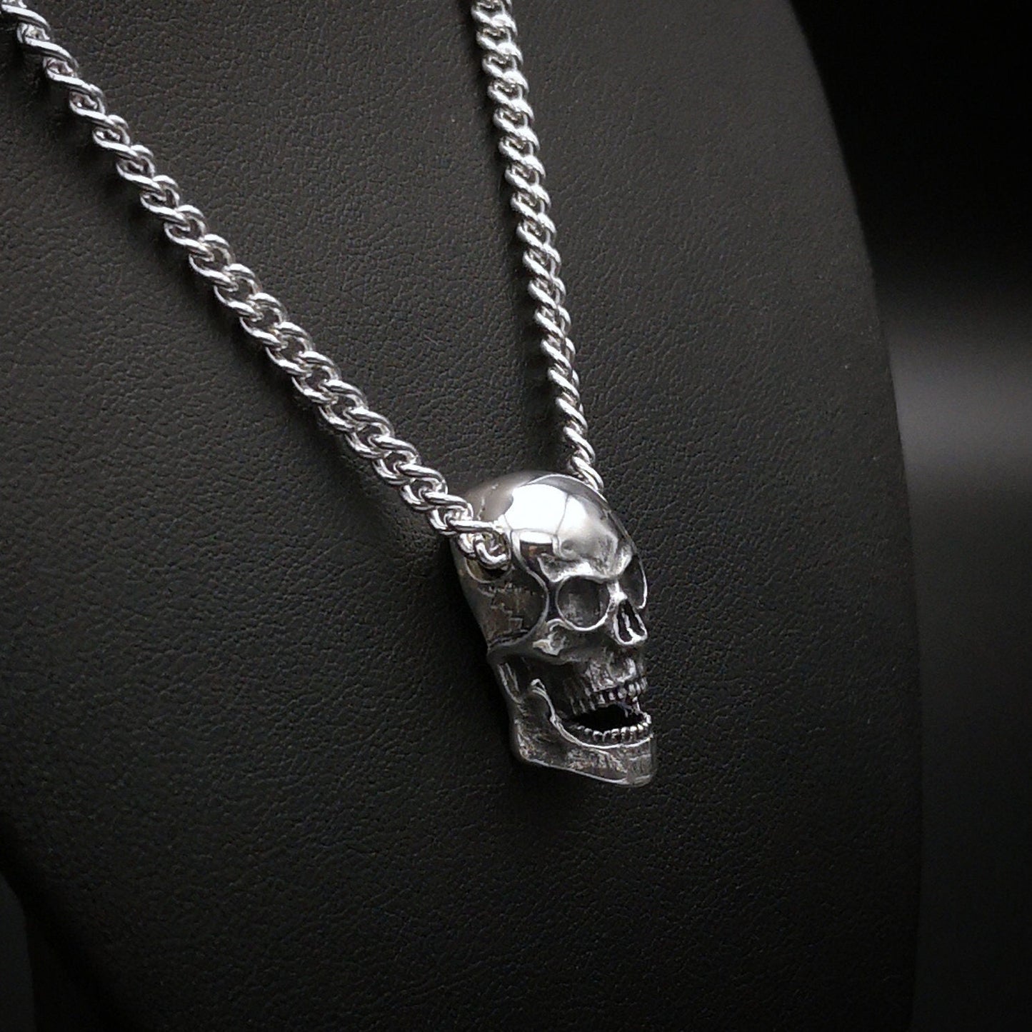 Silver skull pendant on a chain against a dark background