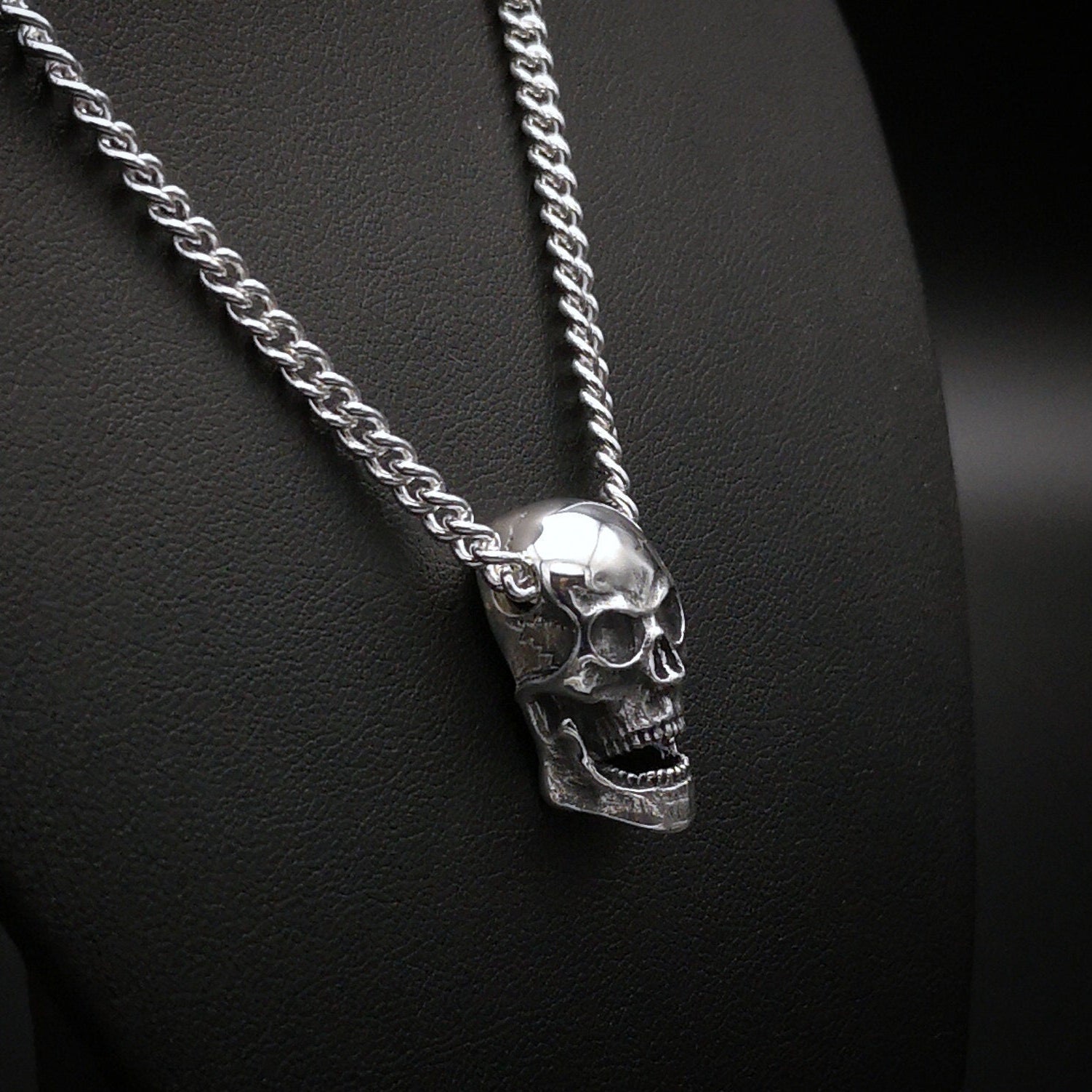 Silver skull pendant on a chain against a dark background