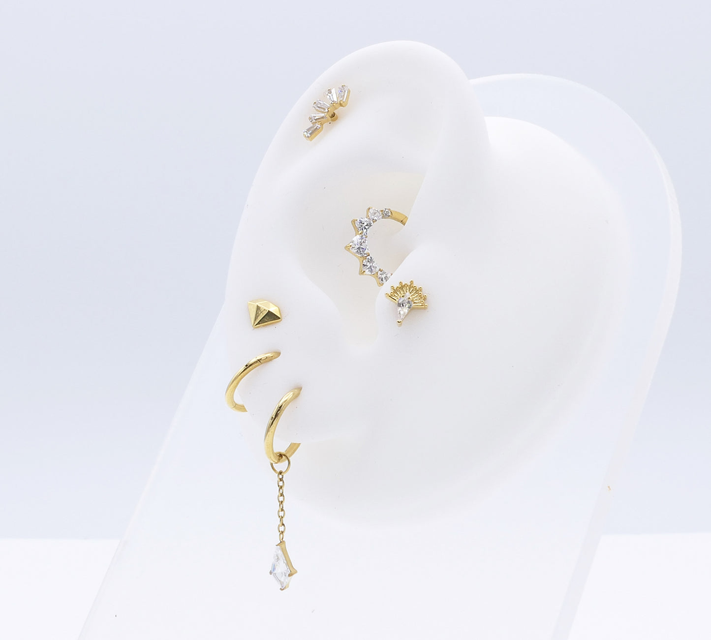 Set of gold earrings on a white earring display stand against a light gray background