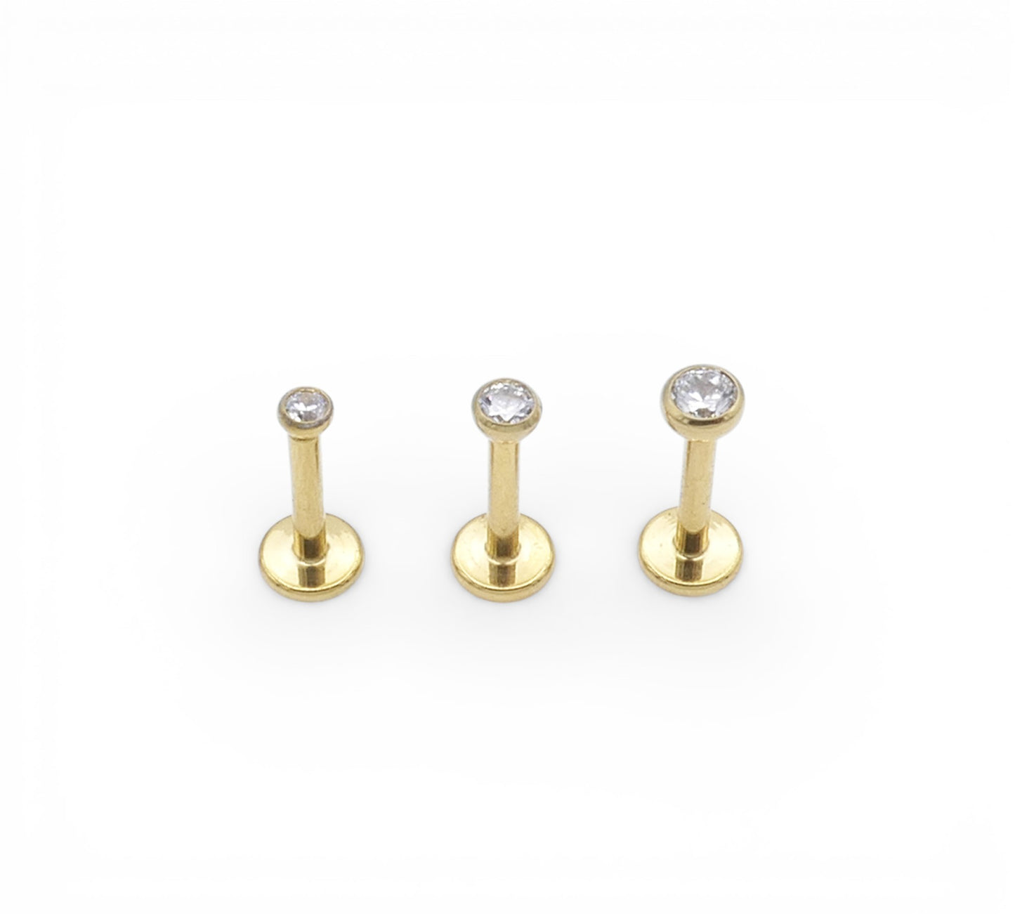 Three gold lip studs with clear gemstones on a white background