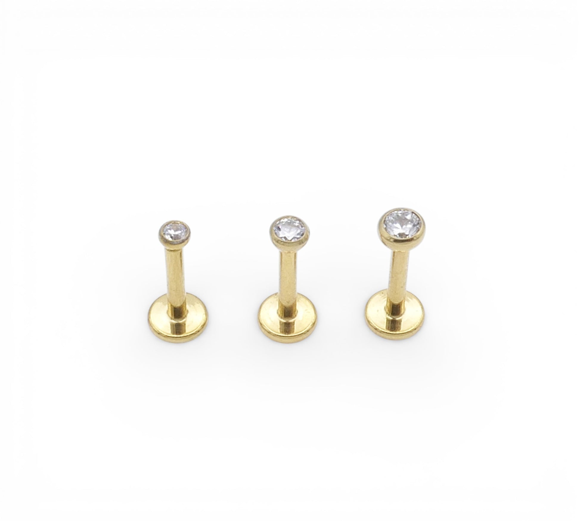 Three gold lip studs with clear gemstones on a white background