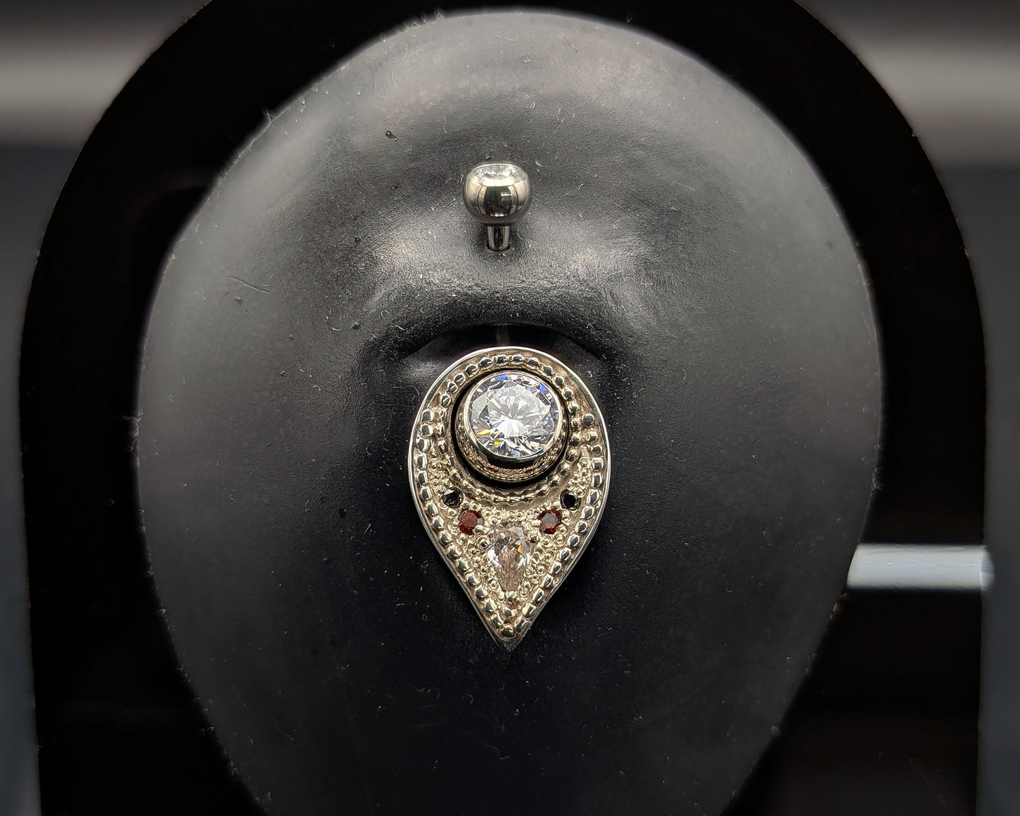 A silver navel shield decorated with granulation, set with gemstones and on a crystal navel bar
