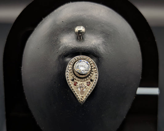 A silver navel shield decorated with granulation, set with gemstones and on a crystal navel bar